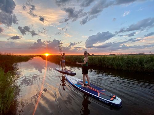 Twee vrouwen die aan het suppen zijn tijdens de zonsondergang