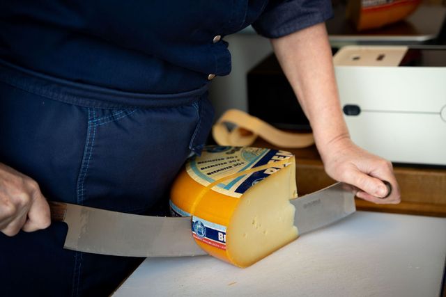 Een persoon snijd een stuk Beemsterkaas.
