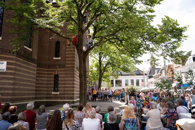 Een act in de boom van Reuring op de Kaasmarkt in Purmerend waar allerlei mensen naar kijken.