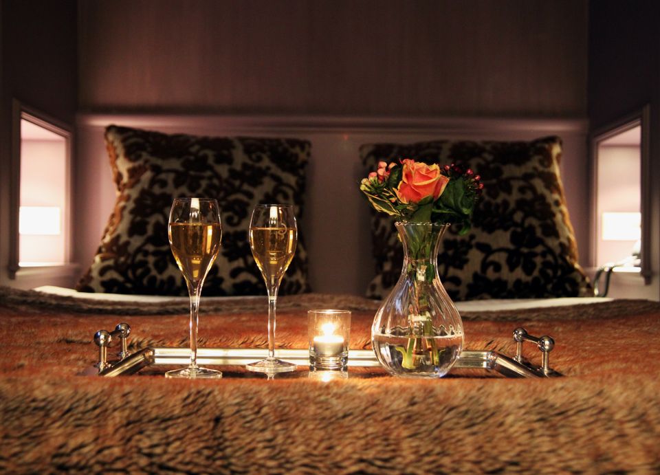 Twee wijnglazen en een bloemetje op een dienblad dat op bed staat