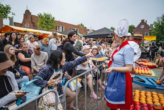 Een vrouw in klederdracht die kaas uitdeelt n op de avondkaasmarkt in Edam