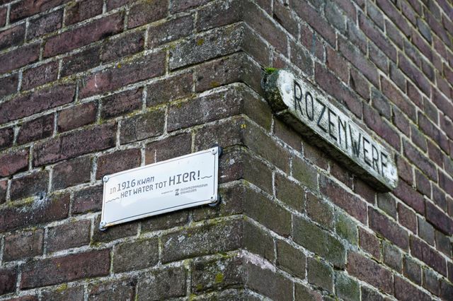 Foto van een muur in de Rozenwerf met daarop het plaatje 'Het water kwam tot hier'. Hierop is te zien tot waar het water kwam tijdens de Watersnood in 1916.
