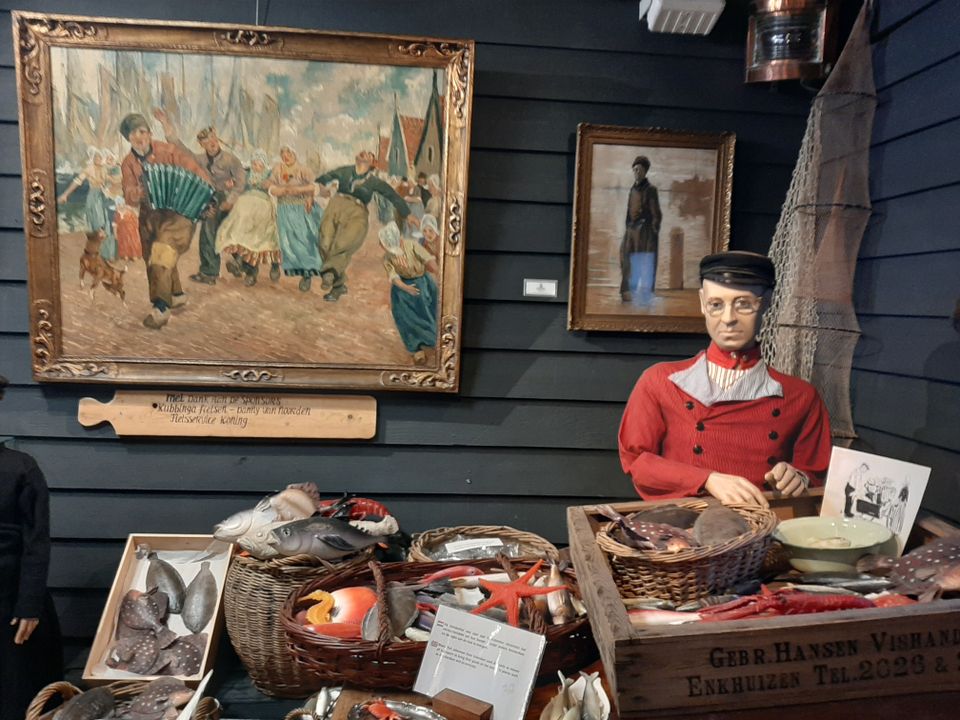 Een pop van een man in Volendamse klederdracht zit achter een stalletje van (nep)vis