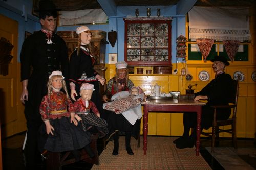 Een foto van het binnenhuisje van het Marker Museum. Het huisje is ingericht in oude Markse stijl, een aantal poppen zijn aangekleed in traditionele Markse klederdracht